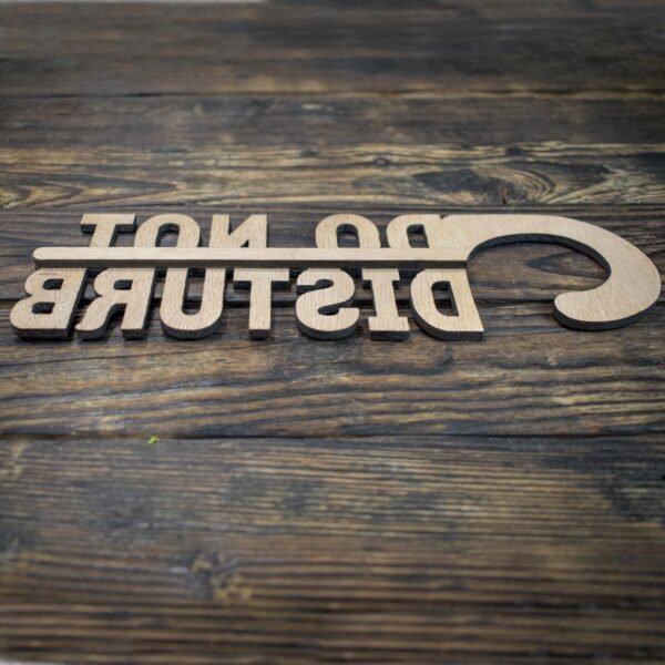 This is a minimalist, laser-cut wooden door hanger used to signal privacy in a hotel or guestroom. The piece is crafted from light natural wood with a smooth, even grain. It has the classic door-hanger shape: a long vertical panel with a curved hook at the top that slips easily over a door handle. What makes this sign unique is that the message is not printed on the wood—the letters themselves are cut out as part of the sign. The text “DO NOT DISTURB” appears in large, bold capital letters that are carved completely through the wood, giving the sign an open, airy look. The letters are thick and sturdy, arranged in three stacked lines, with each word aligned vertically. Because the letters are cut out, the sign has a sculptural, three-dimensional feel, combining both function and design. The overall look is simple, modern, and elegant, making it ideal for boutique hotels, Airbnb stays, spas, or private rooms.