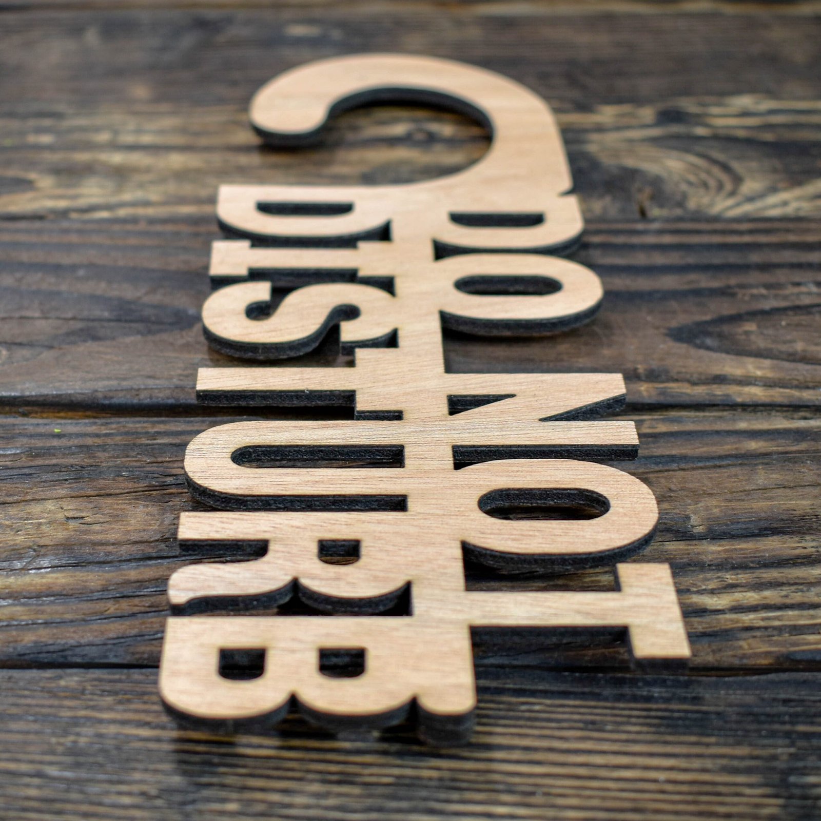 Ξύλινη Πινακίδα για Πόρτα Do not Disturb 4 This is a minimalist, laser-cut wooden door hanger used to signal privacy in a hotel or guestroom. The piece is crafted from light natural wood with a smooth, even grain. It has the classic door-hanger shape: a long vertical panel with a curved hook at the top that slips easily over a door handle. What makes this sign unique is that the message is not printed on the wood—the letters themselves are cut out as part of the sign. The text “DO NOT DISTURB” appears in large, bold capital letters that are carved completely through the wood, giving the sign an open, airy look. The letters are thick and sturdy, arranged in three stacked lines, with each word aligned vertically. Because the letters are cut out, the sign has a sculptural, three-dimensional feel, combining both function and design. The overall look is simple, modern, and elegant, making it ideal for boutique hotels, Airbnb stays, spas, or private rooms.