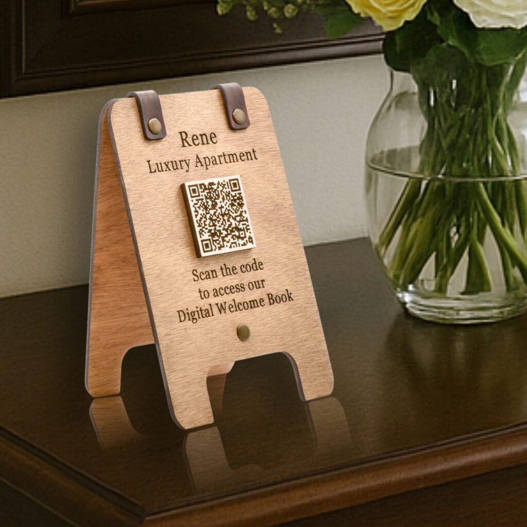 Επιτραπέζια Ξύλινη Πινακίδα Διπλής Όψης με QR Code για Airbnb 'Rene Luxury Apartment'. Η πινακίδα από κόντρα πλακέ 4mm με δερμάτινες λεπτομέρειες, απεικονίζεται πάνω σε σκούρο έπιπλο με βάζο λουλούδια δίπλα, και κατευθύνει τους επισκέπτες στο "Digital Welcome Book" μέσω σάρωσης του QR code.