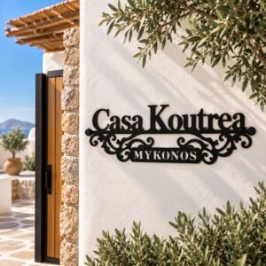 Αρχική 1 Μαύρη μεταλλική επιγραφή Casa Koutrea Mykonos με κομμένο όνομα και διακοσμητικά σχέδια, τοποθετημένη σε λευκό εξωτερικό τοίχο